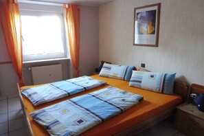 A room with a bed, a window with curtains, a radiator, a framed picture on the wall, and a bedside table with a lamp. - Holiday apartment with 2 bedrooms (Enkirch)