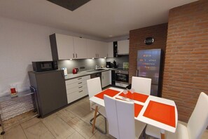 A compact kitchen with white cabinets, a microwave, and a coffee maker. There is a dining table with orange placemats and white chairs. - Sea eagle 22 in Tossens (Butjadingen- Tossens)