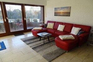 A red sofa, a small table, and a view through a glass door to an outdoor area with chairs. - Sea eagle 22 in Tossens (Butjadingen- Tossens)