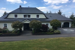 Ein zweistöckiges Haus mit geneigtem Dach, einer Veranda und einer Auffahrt, die zu einer Garage führt.