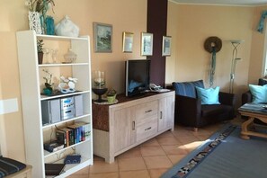 Ein Wohnzimmer mit einer Couch, einem Fernseher, einem Schrank und einem Bücherregal.