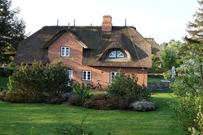 Ein Backsteinhaus mit Strohdach, umgeben von einem gepflegten Garten und einem Fahrrad.
