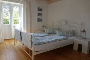 Ein Schlafzimmer mit Bett, Nachttischen, einem Fenster und einer Tür.