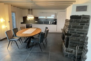 Eine moderne Küche mit Kamin aus Stein, einem Essbereich mit rundem Tisch und Stühlen sowie einer Kücheninsel mit integriertem Backofen.