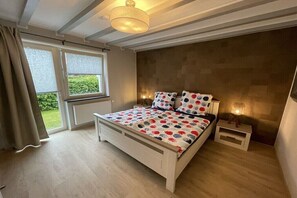Ein Schlafzimmer mit Bett, Nachttischen, einem Fenster mit Vorhängen und einer Deckenleuchte.