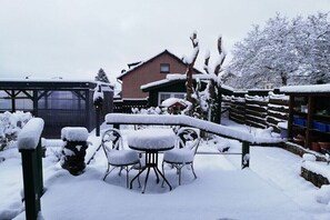 Een besneeud gebied buiten, met een tafel en stoelen, een houten hek en een bakstenen gebouw op de achtergrond.