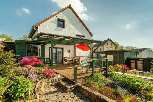 A house with a covered patio, a stone pathway, and a garden with various plants.