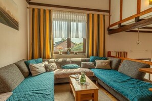 A cozy living room with a large sectional sofa, a small wooden coffee table, and a window with curtains.