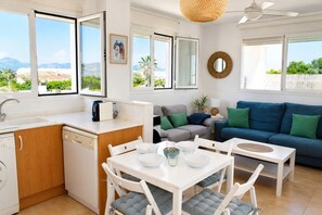 Eine moderne Küche mit Geschirrspüler, einem Esstisch mit Stühlen, einer Couch und einem großen Fenster mit Blick auf Grünflächen und Berge.