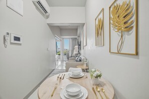 A modern hotel room with a dining area, a view of the city, and a large decorative leaf artwork on the wall. - Luxury BGC Condo • Hotel Vibes • Netflix+Workspace (Taguig)
