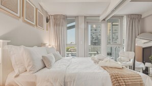 Une chambre d’hôtel avec un grand lit, une chaise, un bureau et une vue sur la ville grâce à de grandes fenêtres.