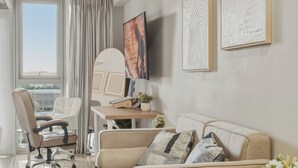 Un salon moderne avec un canapé, un bureau, une chaise, un téléviseur et des œuvres d’art accrochées aux murs.