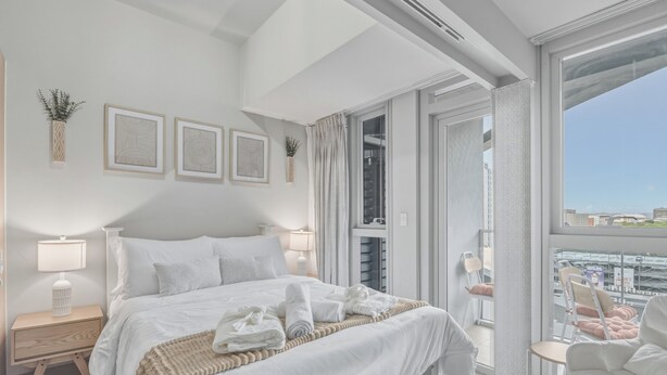 Une chambre d’hôtel moderne avec un grand lit, une table de chevet, une chaise et un balcon offrant une vue agréable.