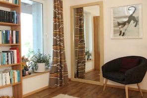 Een kamer met een boekenkast, een stoel, een spiegel en een ingelijst schilderij aan de muur.