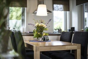 Een eethoek met een houten tafel, zwarte stoelen, een vaas met bloemen en een hanglamp.