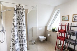 Een badkamer met douche, toilet en een glazen scheidingswand. Er is een plank met opgevouwen handdoeken en een ladder.