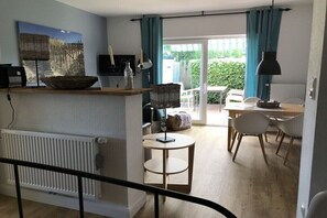 Ein modernes Wohnzimmer mit Essbereich, einem großen Fenster mit Vorhängen und Blick auf einen Garten.