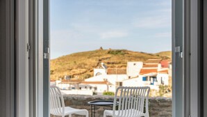 Puerta abierta con vistas a una colina, sillas blancas y una pequeña mesa.