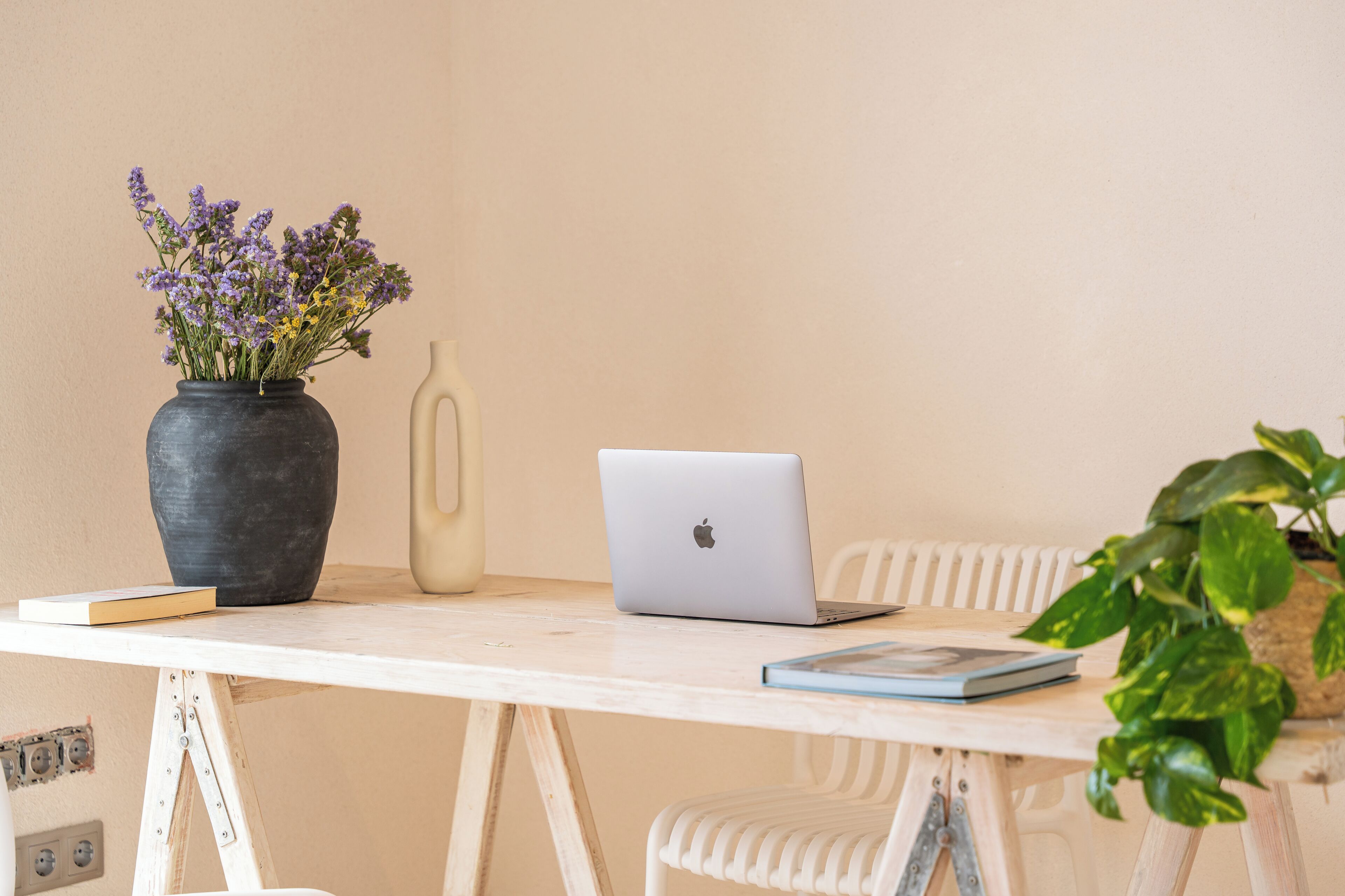 A white table with a laptop, a vase of flowers, and a book.
