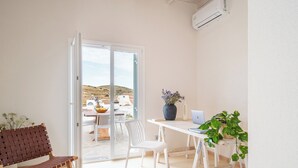 Una habitación con una mesa blanca, una silla blanca, un banco tejido marrón, una computadora portátil y una planta en maceta.