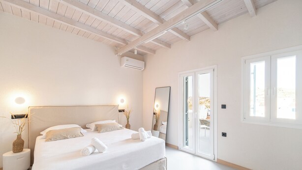 Un dormitorio con una cama grande, mesitas de noche, un espejo y un ventanal corredero que da a un espacio exterior.