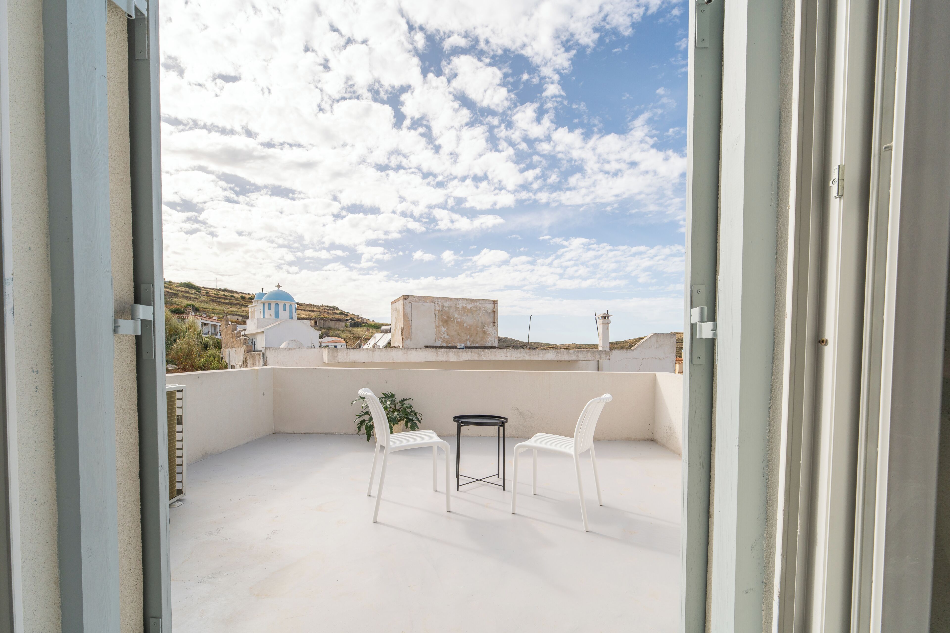 An open balcony with a table and chairs, a view of a church, and a clear sky.