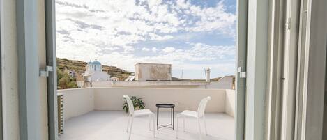An open balcony with a table and chairs, a view of a church, and a clear sky.