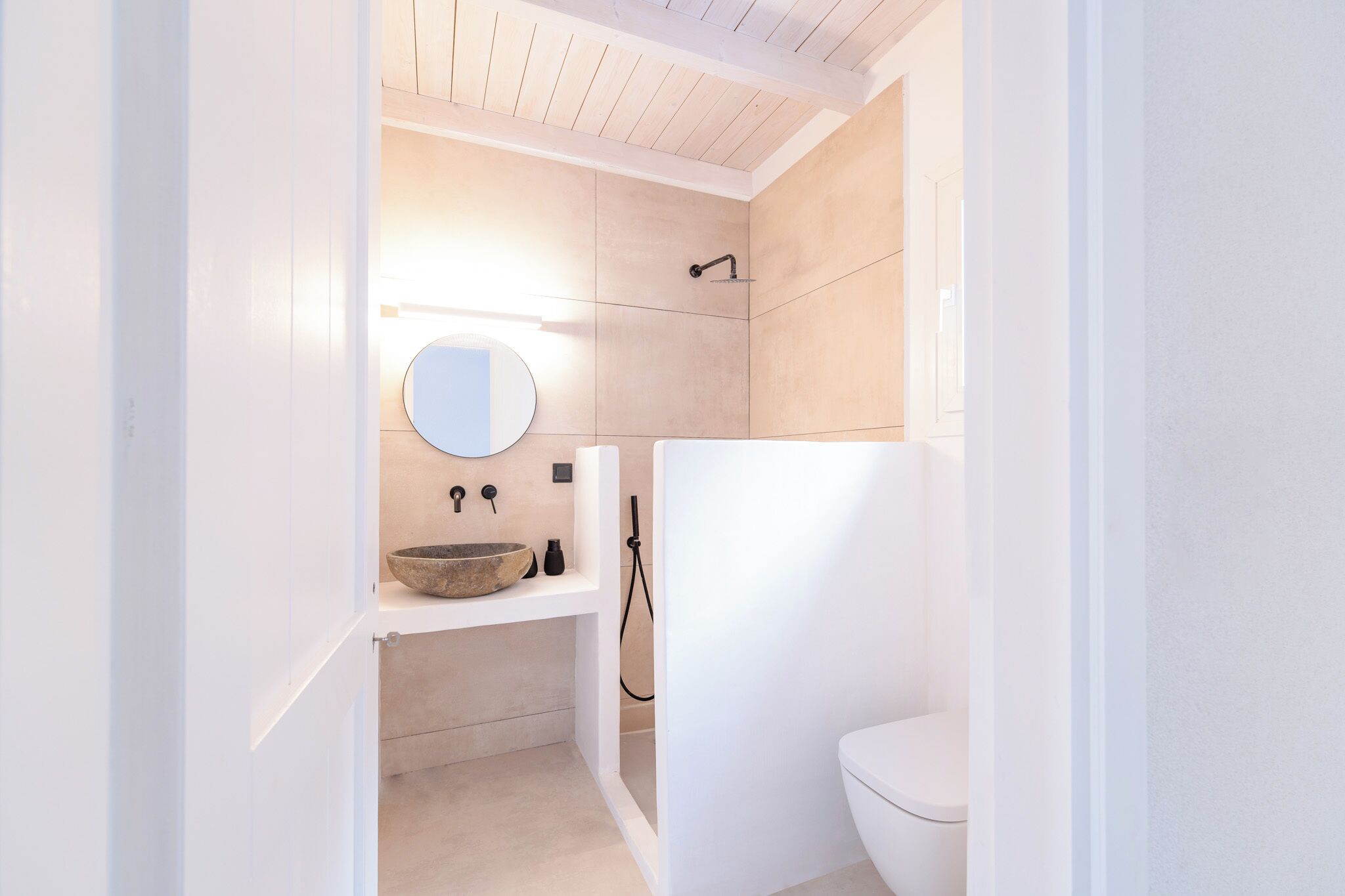 A modern bathroom with a white sink, a round mirror, and a toilet.