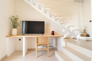 Un interior moderno con una escalera, un televisor de pantalla plana, una silla de mimbre y una planta en maceta.