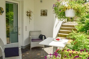 Eine Terrasse mit Korbmöbeln, einem weißen Tisch und einer Topfpflanze.
