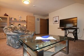Ein Wohnzimmer mit einem Glastisch, einer Couch, einem Fernseher und einem Bücherregal.