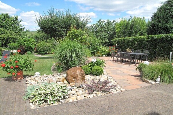 Ein Garten mit gepflasterter Terrasse, Tisch und Stühlen.