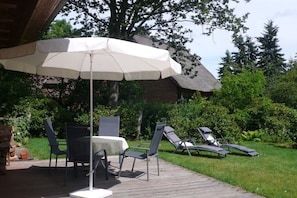 A patio with a table and chairs, a lounge chair, and a large umbrella. - Holiday home in Trebel with swimming pool (Trebel)