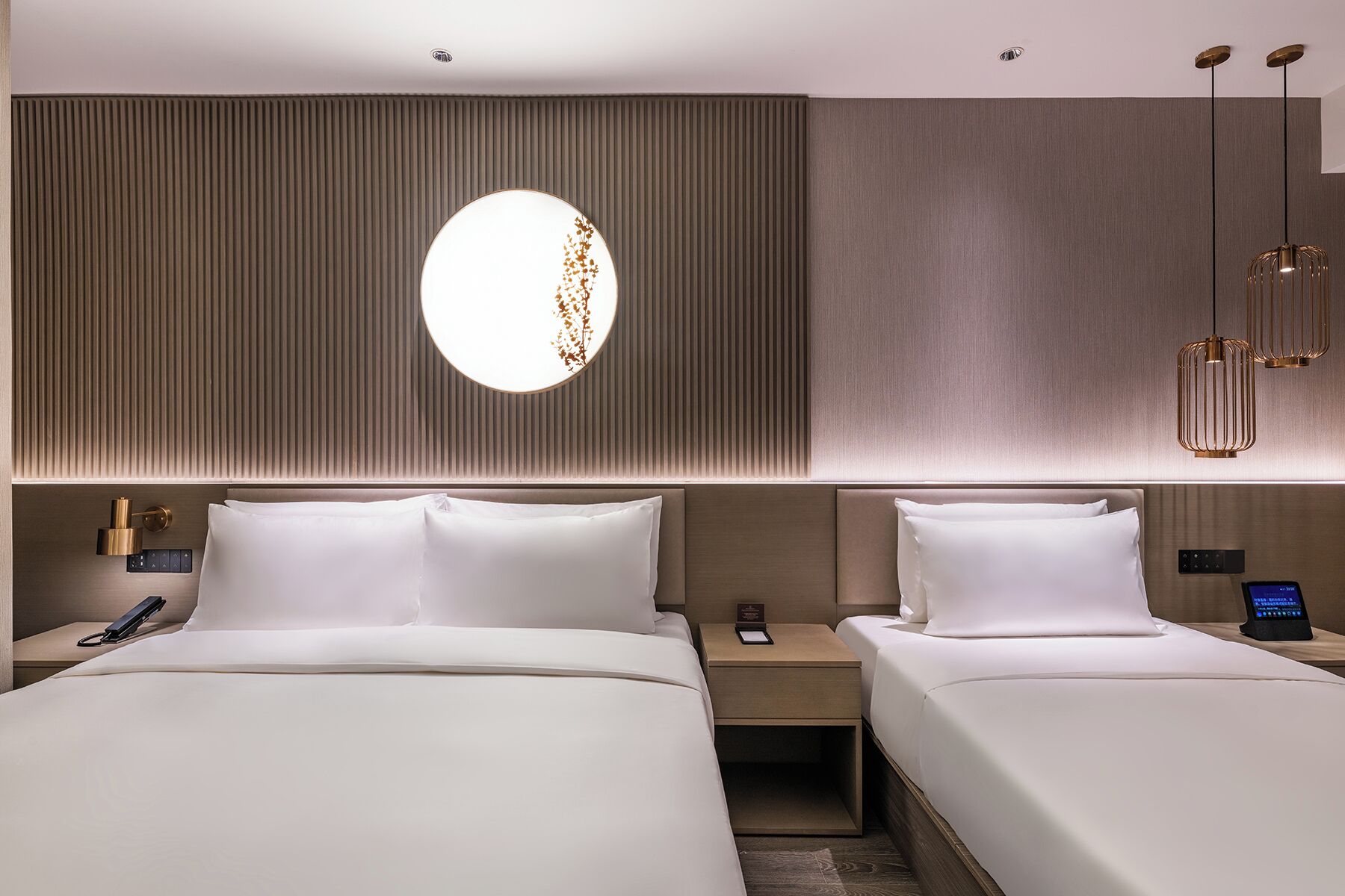 Habitación de hotel con dos camas, un espejo redondo, una mesita de noche con teléfono y una lámpara de pared.