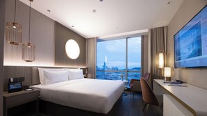 A modern hotel room with a large bed, a desk, a chair, a TV, and a view of a cityscape. - Crystal Hotel Qingdao MixC Shandong Road (Qingdao)