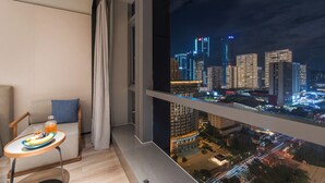 A balcony with a cityscape view at night, a small table with a plate of fruit, and a cushioned chair. - Crystal Hotel Qingdao MixC Shandong Road (Qingdao)