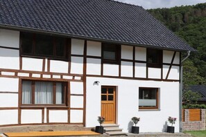 Ein zweigeschossiges Gebäude mit weißer Fassade und dunklen Ziegeldächern, das ein Fensterdesign mit Holzrahmen und einen Hauseingang mit einer Tür aufweist.