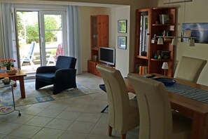 Ein Wohnzimmer mit Sofa, Fernseher, Bücherregal und Essbereich.