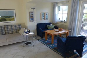 Ein Wohnzimmer mit einer Couch, einem Couchtisch, einem Sessel, einer Lampe und gerahmten Bildern an der Wand.