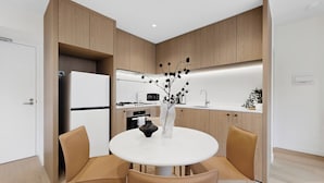 Una cocina moderna con armarios de madera, un refrigerador blanco, una mesa de comedor con sillas y un florero con ramas.