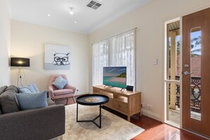 A living room with a sofa, a chair, a coffee table, a TV, and a door leading outside. - Family-Friendly 4-Bed Home with Parking (Seacombe Gardens)
