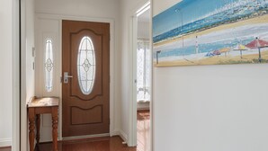 A hallway with a wooden door, a small table, and a painting of a beach scene. - Family-Friendly 4-Bed Home with Parking (Seacombe Gardens)