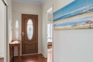 A hallway with a wooden door, a small table, and a painting of a beach scene. - Family-Friendly 4-Bed Home with Parking (Seacombe Gardens)