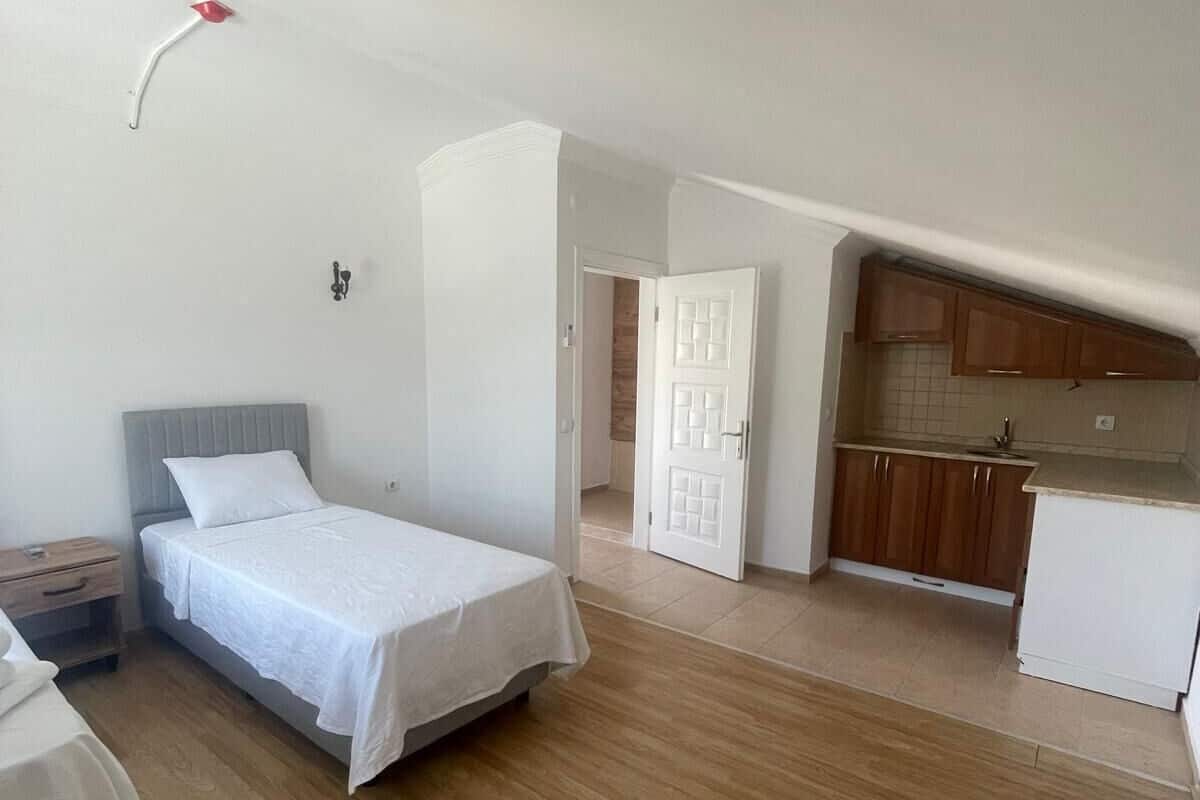 Un dormitori amb un llit, una tauleta de nit i una cuineta que disposa d'armaris de fusta i un taulell blanc.