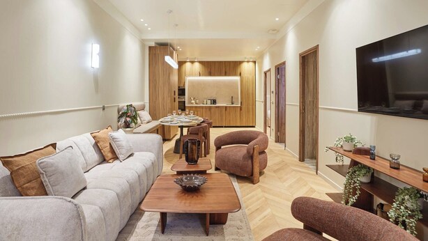 Un salon moderne avec un canapé, des fauteuils, une table basse, un téléviseur et, au fond, un coin cuisine.