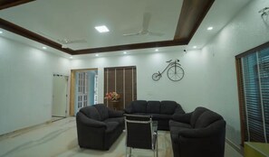 A living room with a sectional sofa, a coffee table, a ceiling fan, and a wall-mounted bicycle decoration. - The Wanderlust stays (Dehradun)