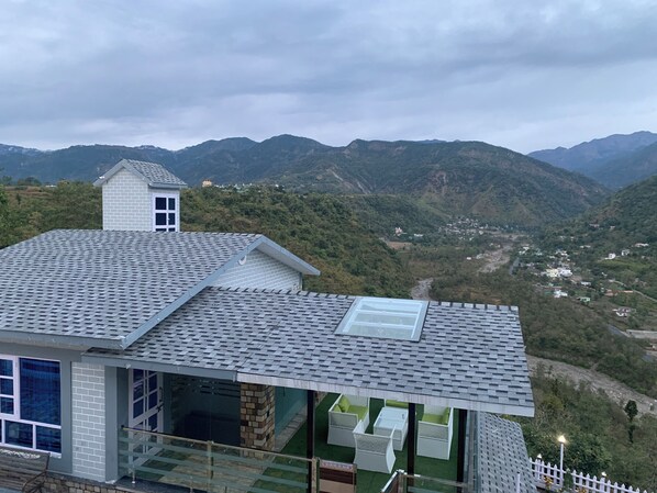 A modern building with a sloped roof, large windows, and a view of a valley with mountains. - The Wanderlust stays (Dehradun)