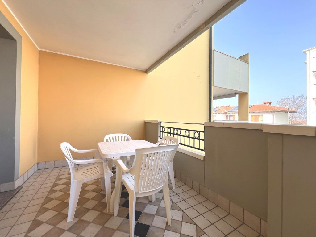 A balcony with a checkered floor, a table with chairs, and a view of buildings through a window.