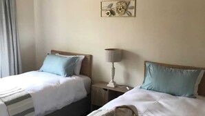 A hotel room with two beds, a nightstand with a lamp, a decorative wall piece, and a window with curtains.