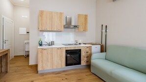 A compact kitchen with wooden cabinets, a built-in oven, and a light green sofa in a modern apartment. - GuestHost - Cozy Balcony Flat X3 near the Sea (Francavilla al Mare)